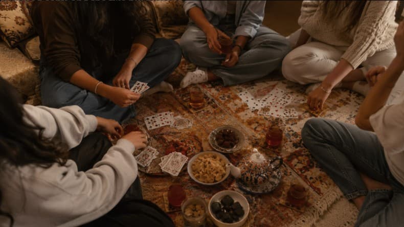 Roommates sharing tea around a card game in their living room